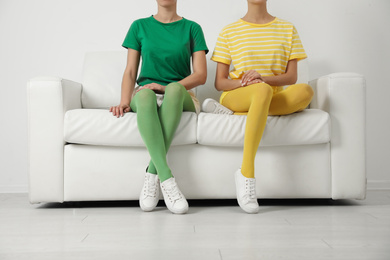 Women wearing bright tights sitting on sofa indoors, closeup