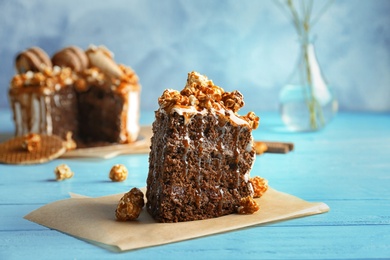 Photo of Piece of delicious homemade cake with caramel sauce and popcorn on table