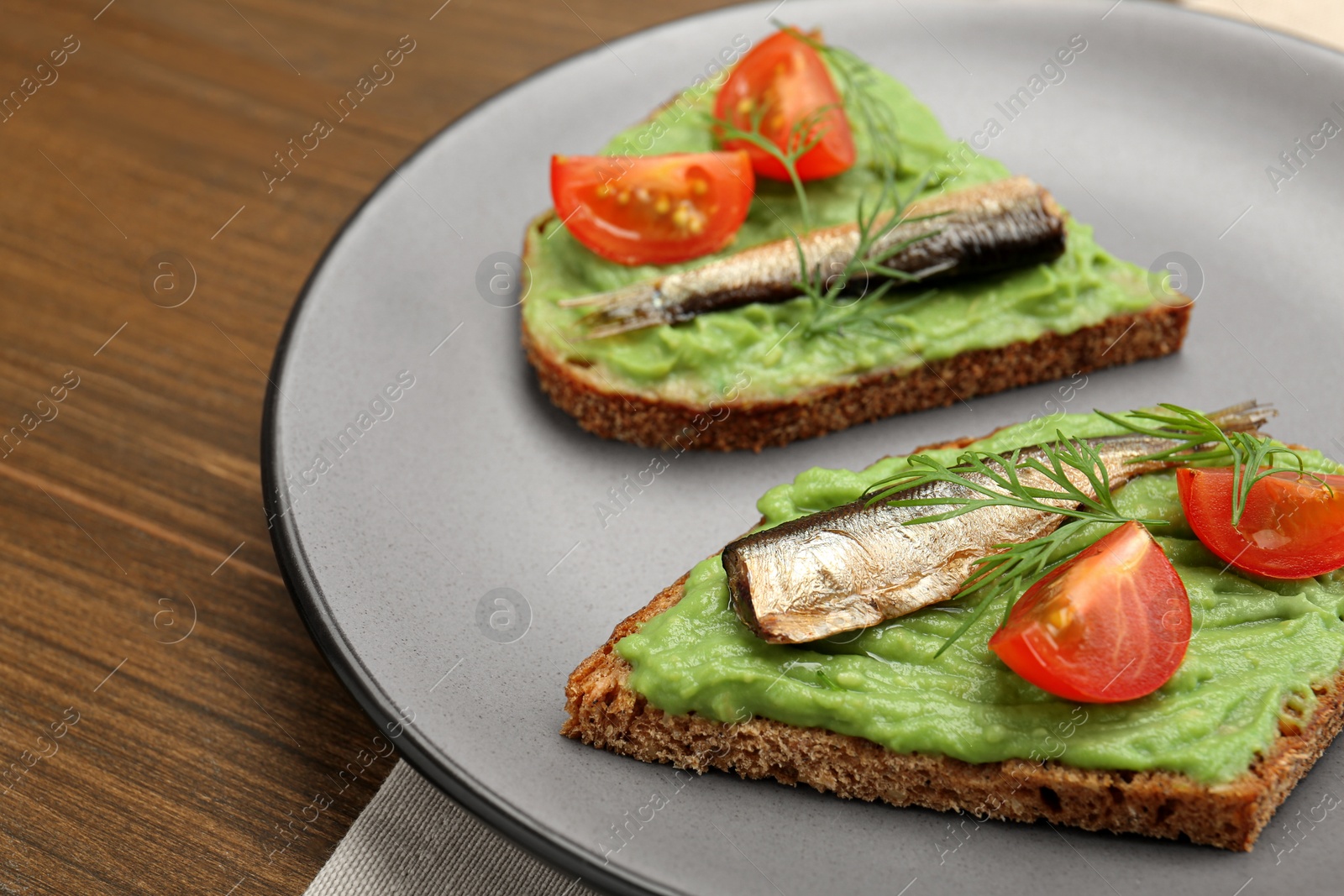 Photo of Delicious sandwiches with sprats, tomatoes, avocado puree and dill on wooden table, closeup. Space for text