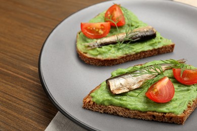 Photo of Delicious sandwiches with sprats, tomatoes, avocado puree and dill on wooden table, closeup. Space for text