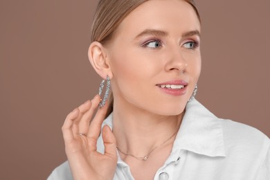 Beautiful young woman with elegant jewelry on light brown background