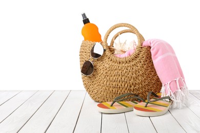 Stylish bag with beach accessories on wooden table against white background