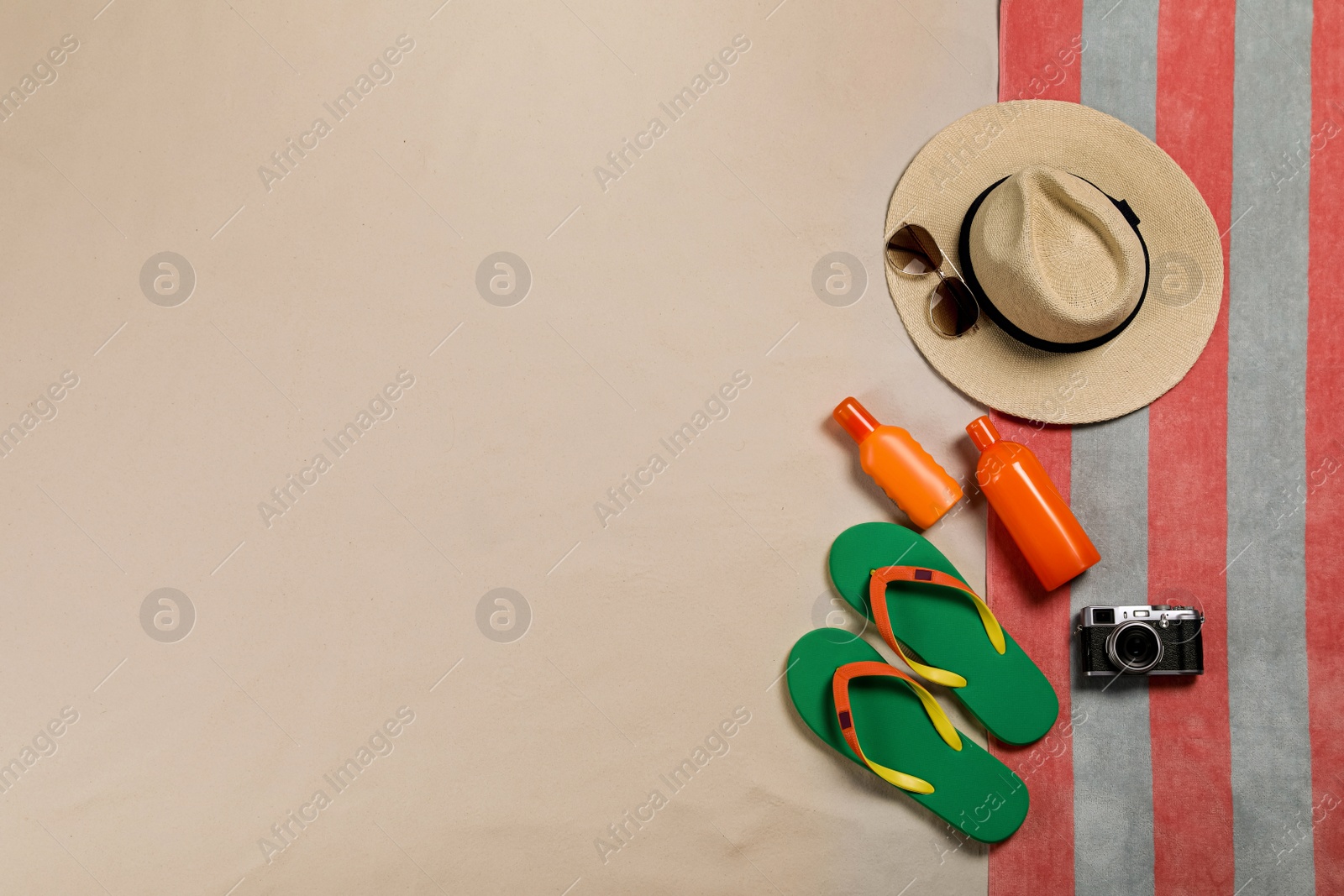 Photo of Beach towel, hat, sunglasses, camera, sunscreen and flip flops on sand, flat lay. Space for text