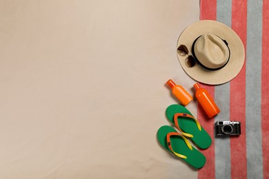 Photo of Beach towel, hat, sunglasses, camera, sunscreen and flip flops on sand, flat lay. Space for text
