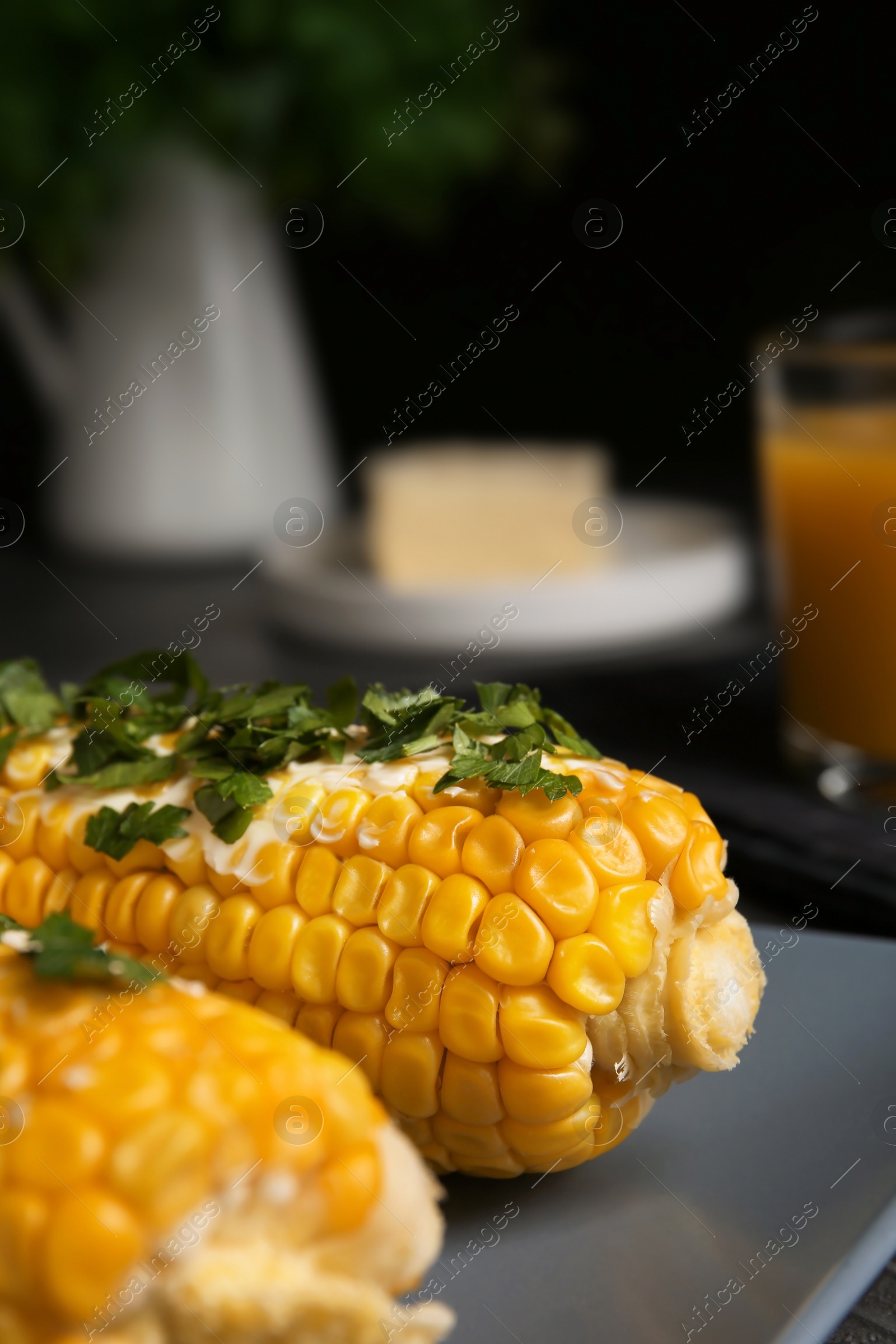 Photo of Delicious boiled corn cobs with butter and parsley on gray table, closeup