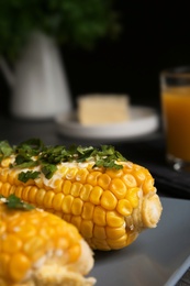 Photo of Delicious boiled corn cobs with butter and parsley on gray table, closeup