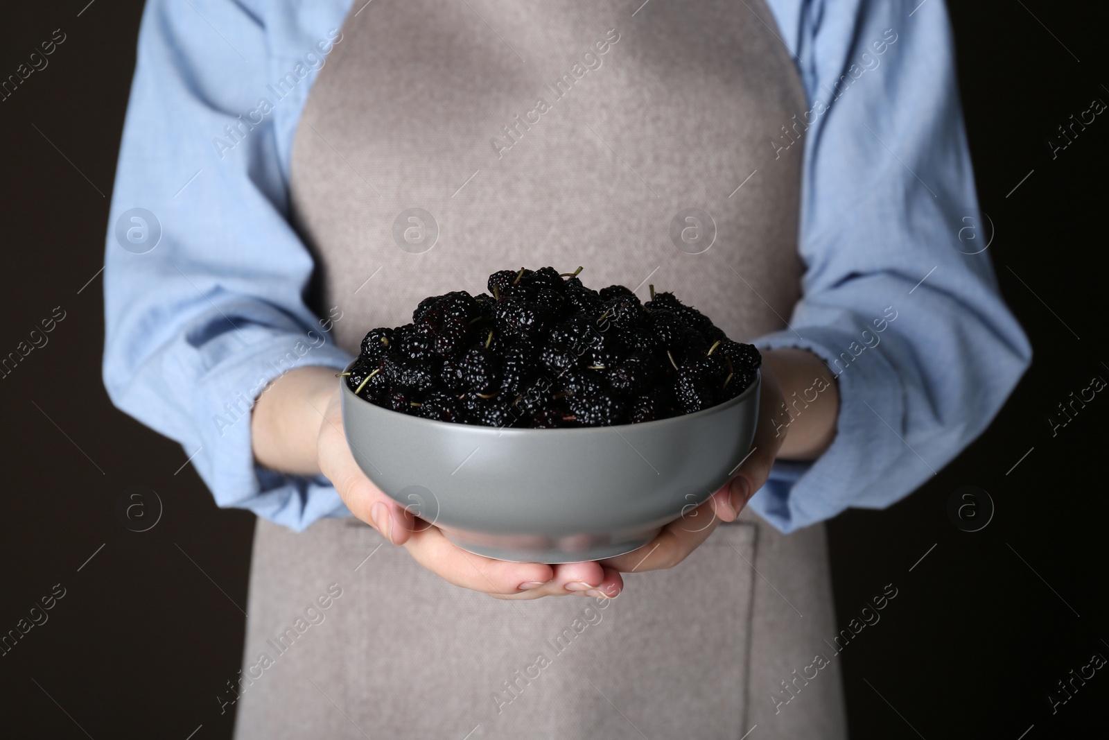 Photo of Woman holding bowl of fresh ripe mulberries on black background, closeup