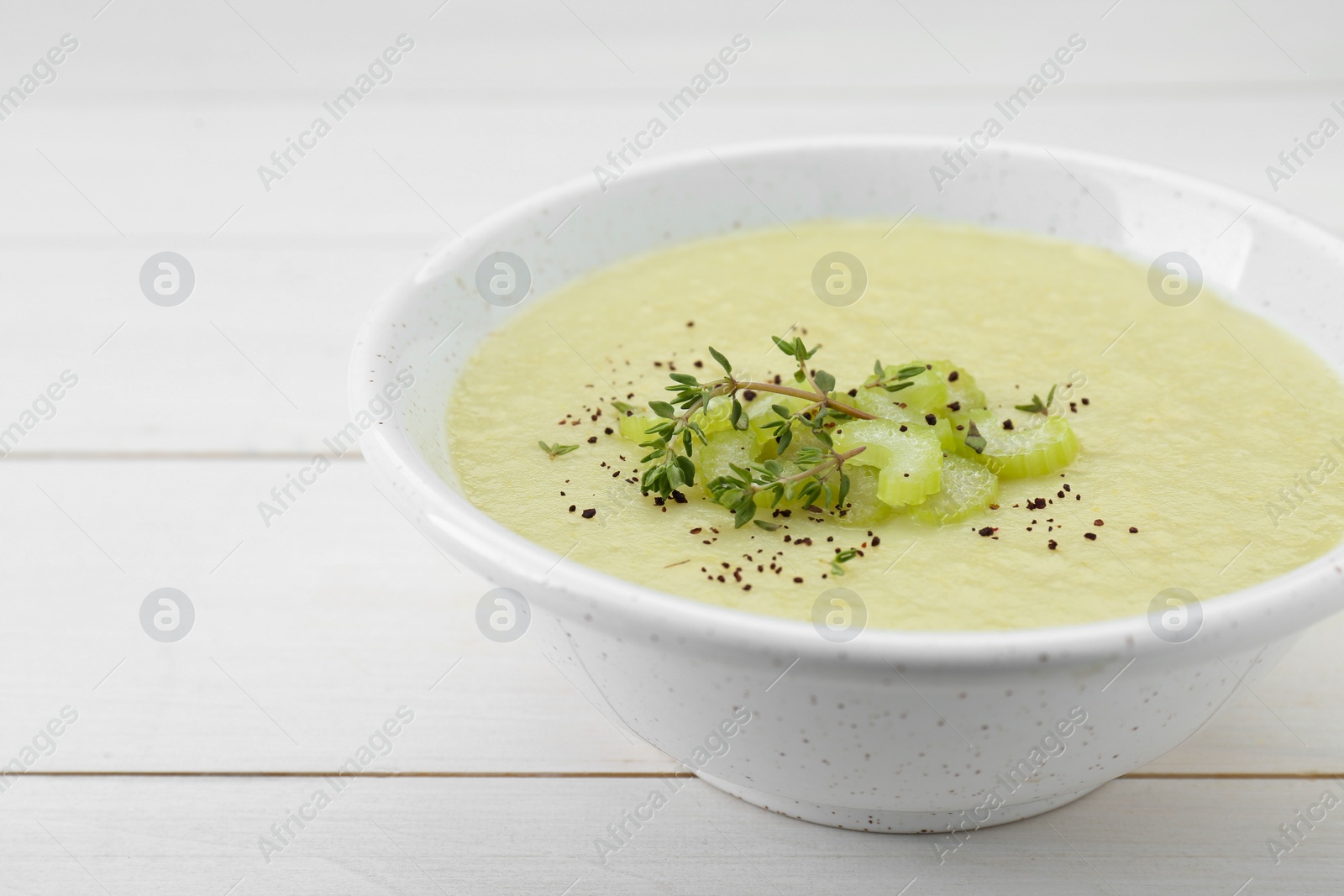 Photo of Bowl of delicious celery soup on white wooden table, closeup. Space for text