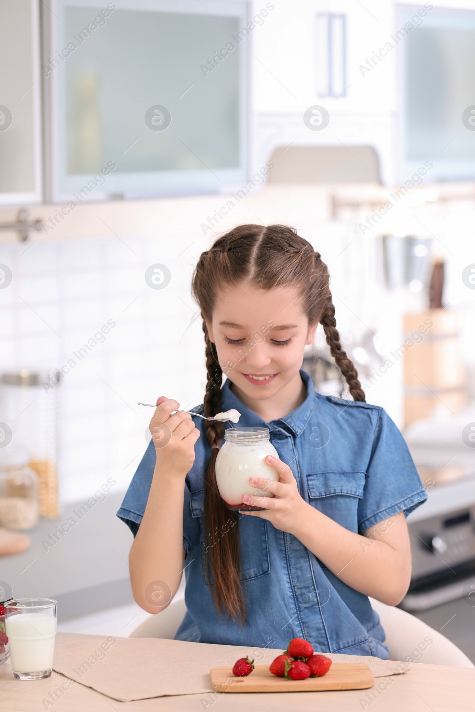 Photo of Cute girl eating tasty yogurt at table in kitchen