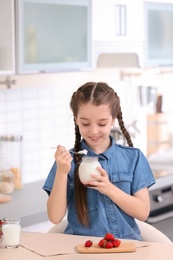 Cute girl eating tasty yogurt at table in kitchen