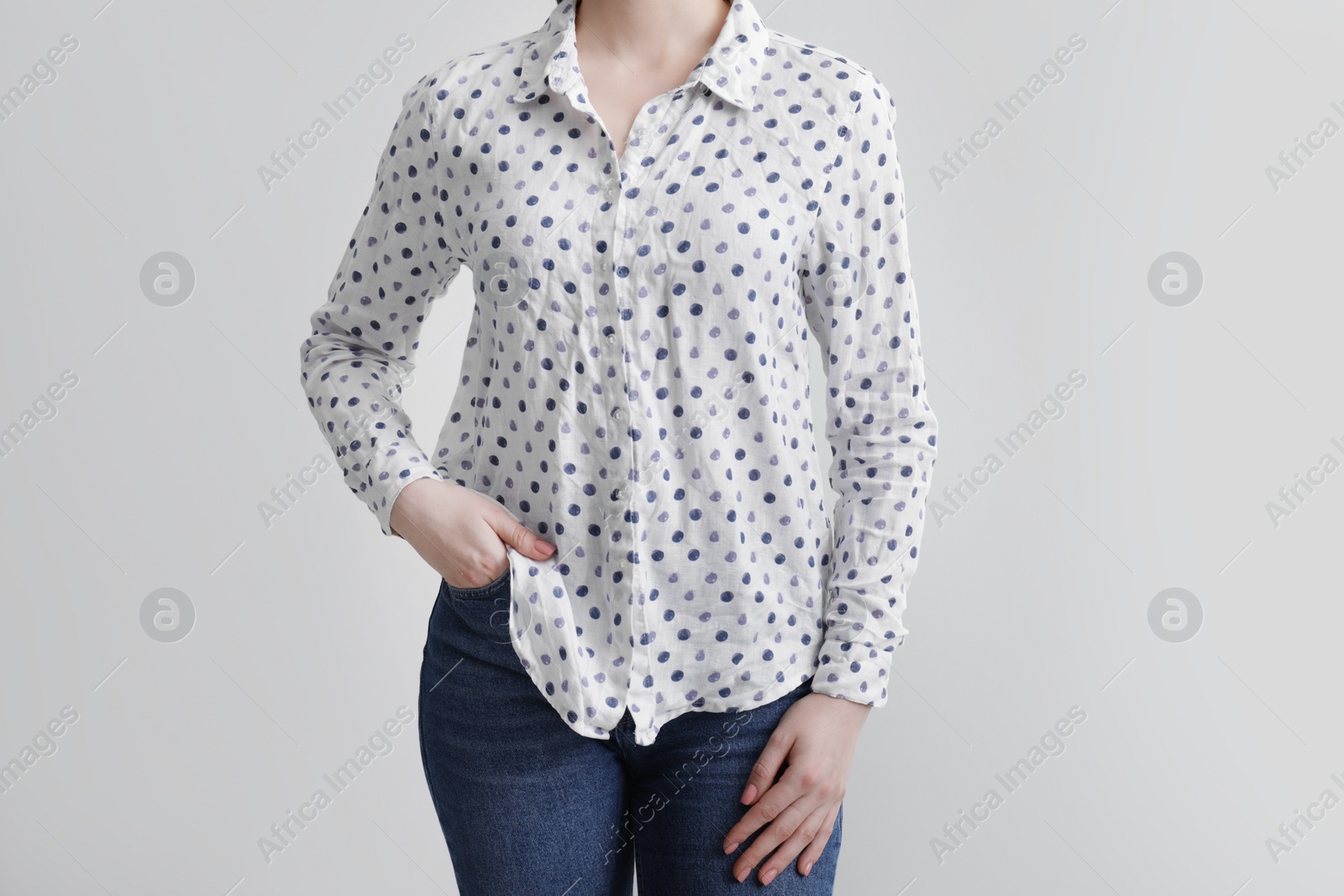 Photo of Woman wearing wrinkled white polka dot blouse on light grey background, closeup