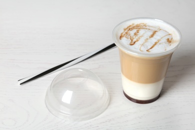 Photo of Plastic cup of tasty caramel macchiato on wooden table