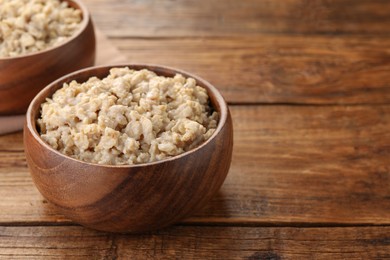 Photo of Tasty boiled oatmeal in bowl on wooden table, closeup. Space for text