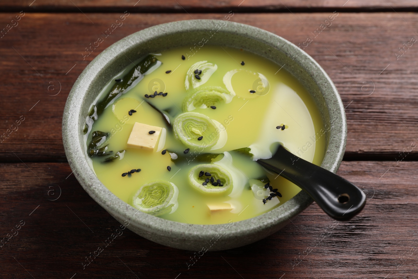 Photo of Bowl of delicious miso soup with tofu and spoon on wooden table, closeup