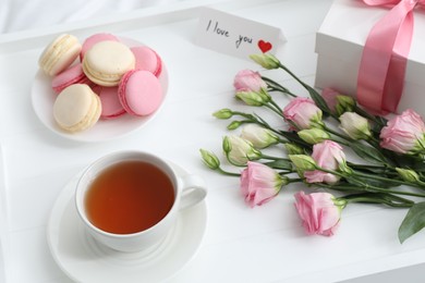 Photo of Tasty breakfast served in bed. Delicious macarons, tea, gift box, flowers and I Love You card on tray