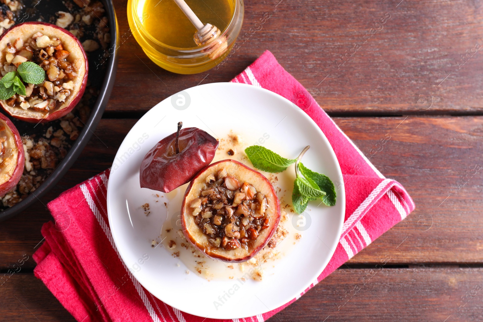 Photo of Tasty baked apples with nuts, honey and mint in dishware on wooden table, flat lay