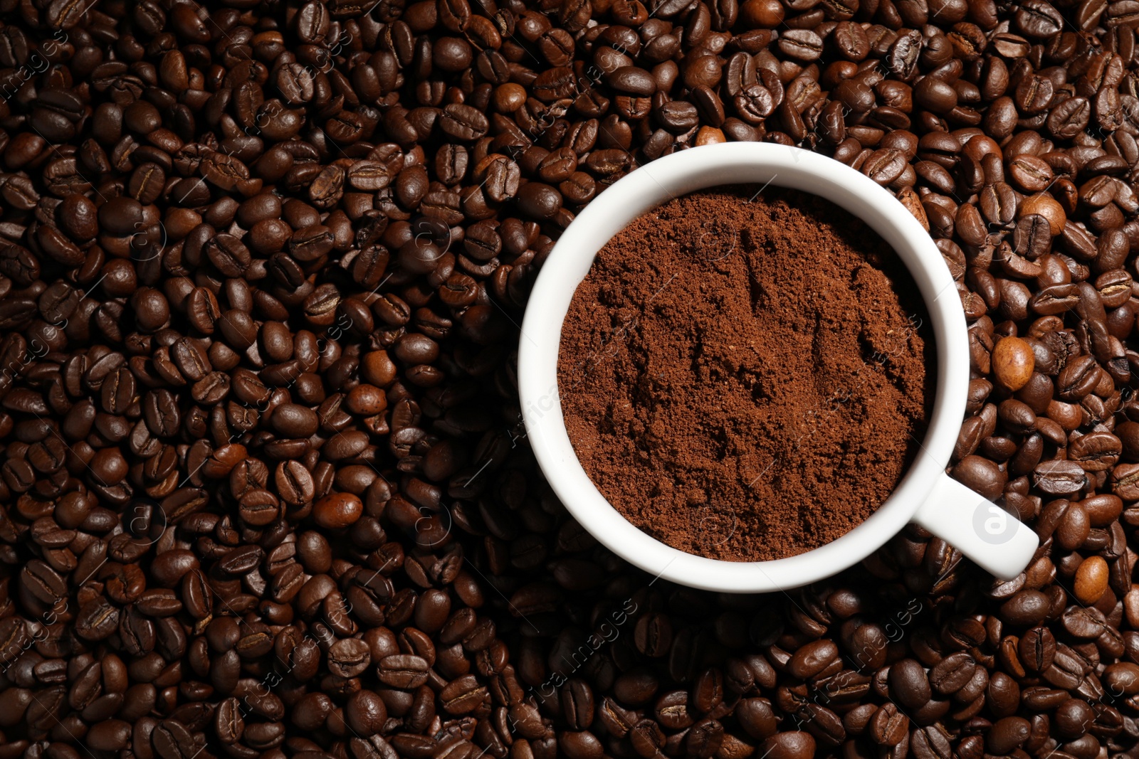 Photo of Cup with ground coffee on roasted beans, top view. Space for text