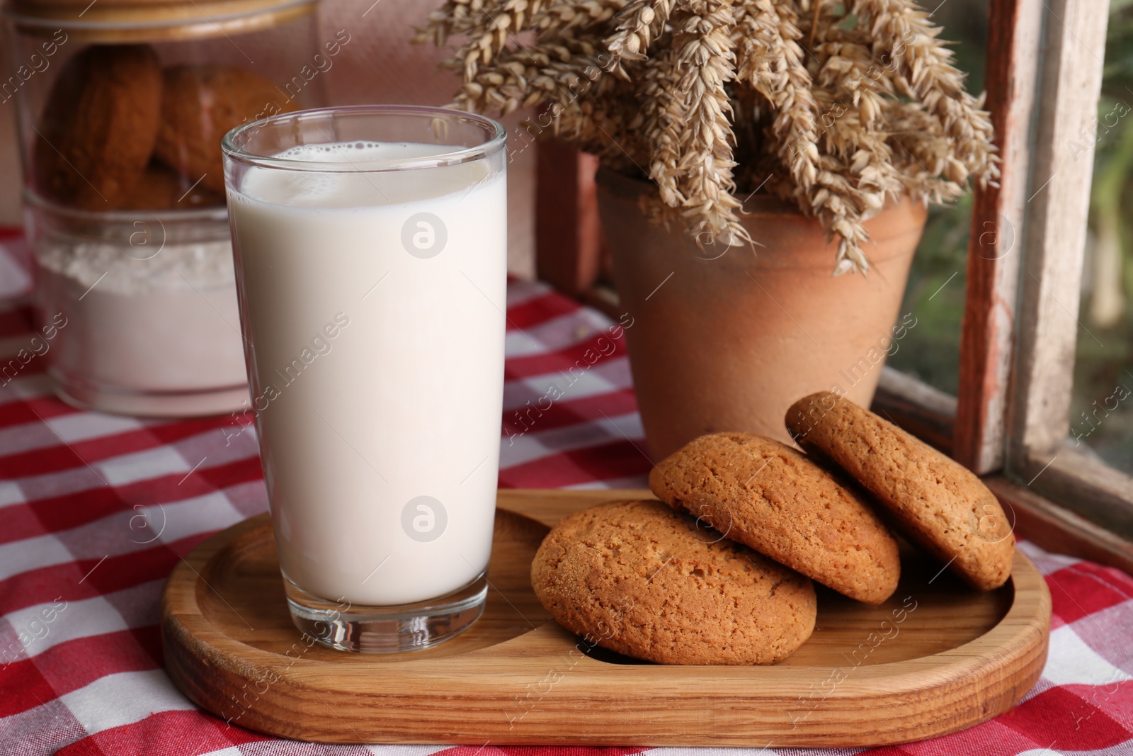 Photo of Glass of milk with cookies on red checkered tablecloth indoors