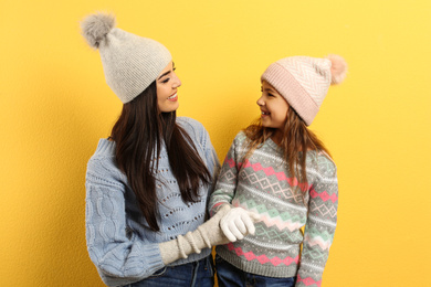 Photo of Happy mother and daughter in warm clothes on yellow background. Winter vacation