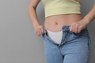 Woman trying to put on tight jeans against light grey background, closeup. Space for text