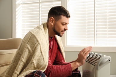 Man warming hands near electric heater at home