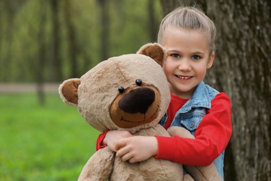 Photo of Cute little girl with teddy bear outdoors