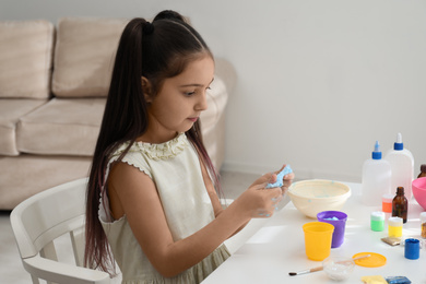 Cute little girl making DIY slime toy at table in room