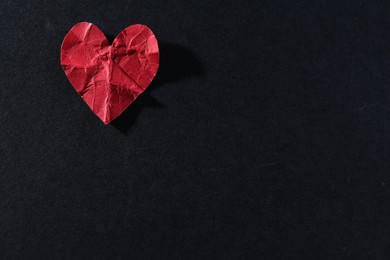 Photo of Red crumpled paper heart on black background, top view with space for text. Breakup concept