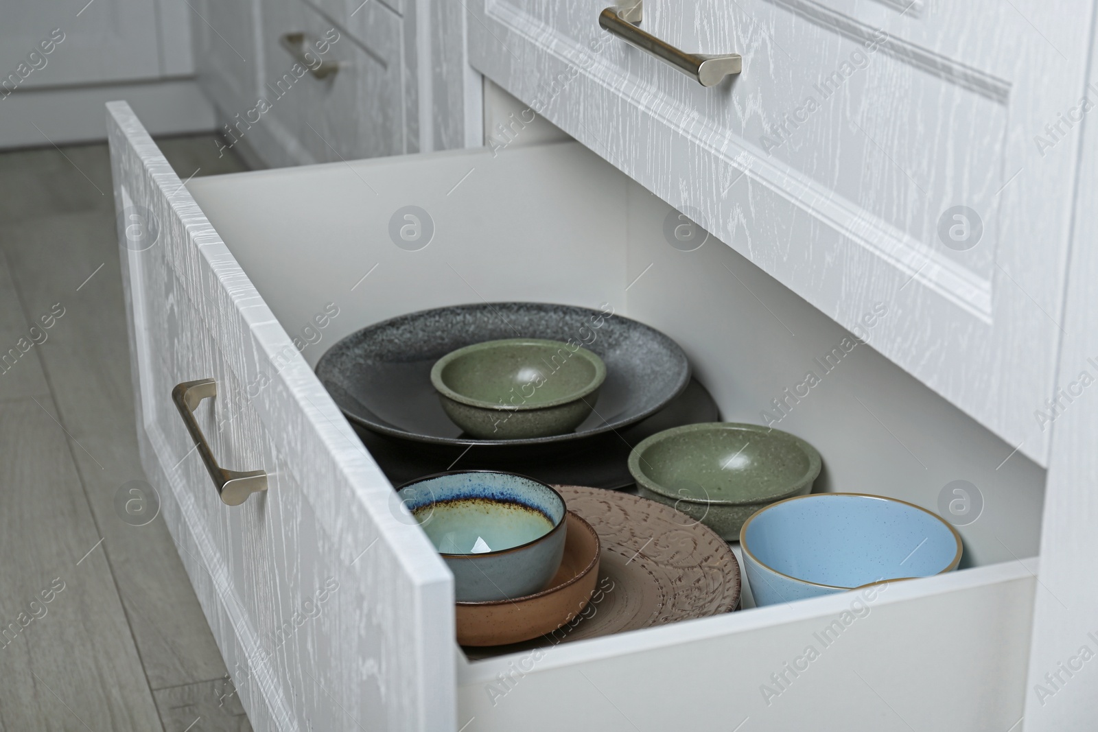 Photo of Open drawers with different plates and bowls in kitchen, closeup