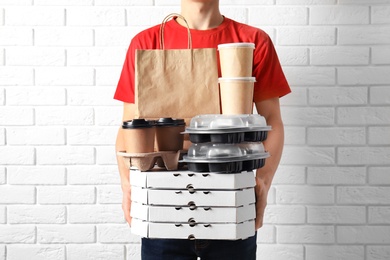Courier with stack of orders near white brick wall. Food delivery service