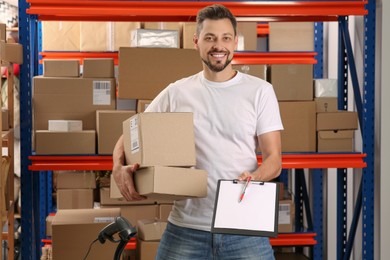 Photo of Post office worker with clipboard and parcels near rack indoors