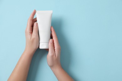 Woman with tube of hand cream on light blue background, top view. Space for text