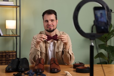 Photo of Fashion blogger showing men's accessories while recording video at home