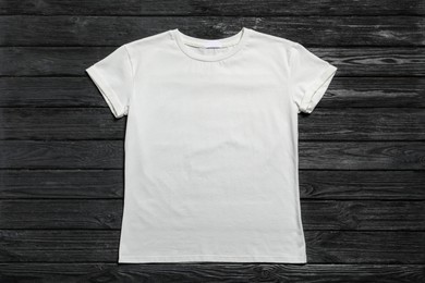 Stylish white t-shirt on black wooden background, top view