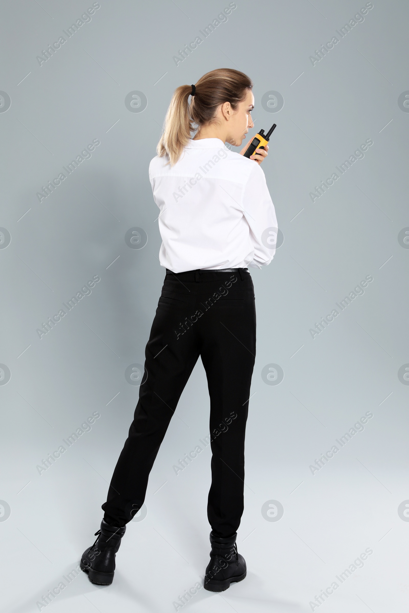 Photo of Female security guard in uniform using portable radio transmitter on grey background