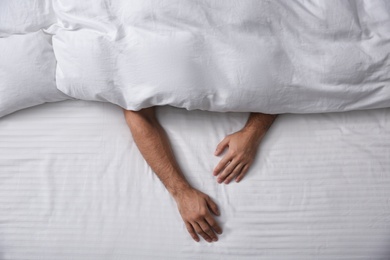 Man sleeping under soft blanket in bed at home, top view