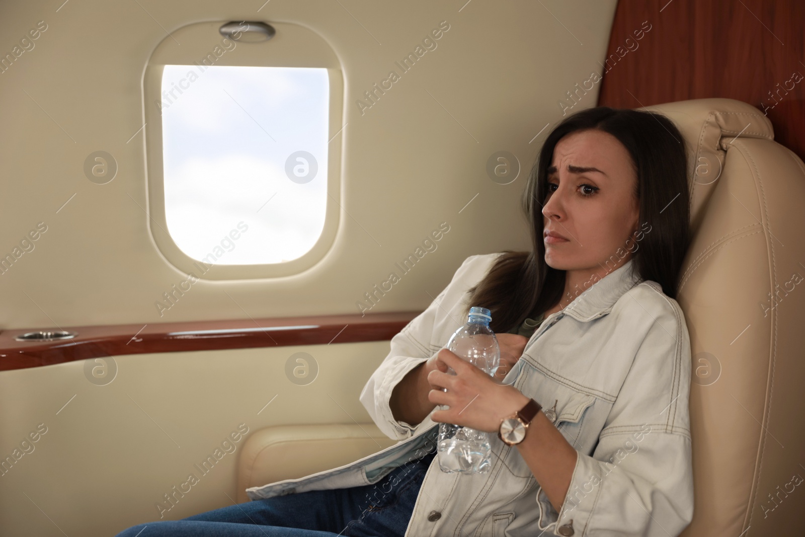 Photo of Nervous young woman with bottle of water in airplane. Aviophobia concept