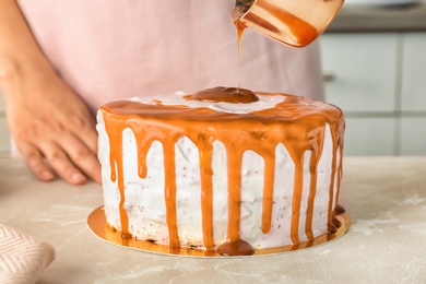 Photo of Young woman applying caramel sauce onto delicious homemade cake at table