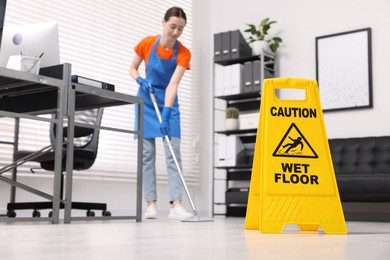 Photo of Cleaning service worker washing floor with mop in office, focus on wet floor sign