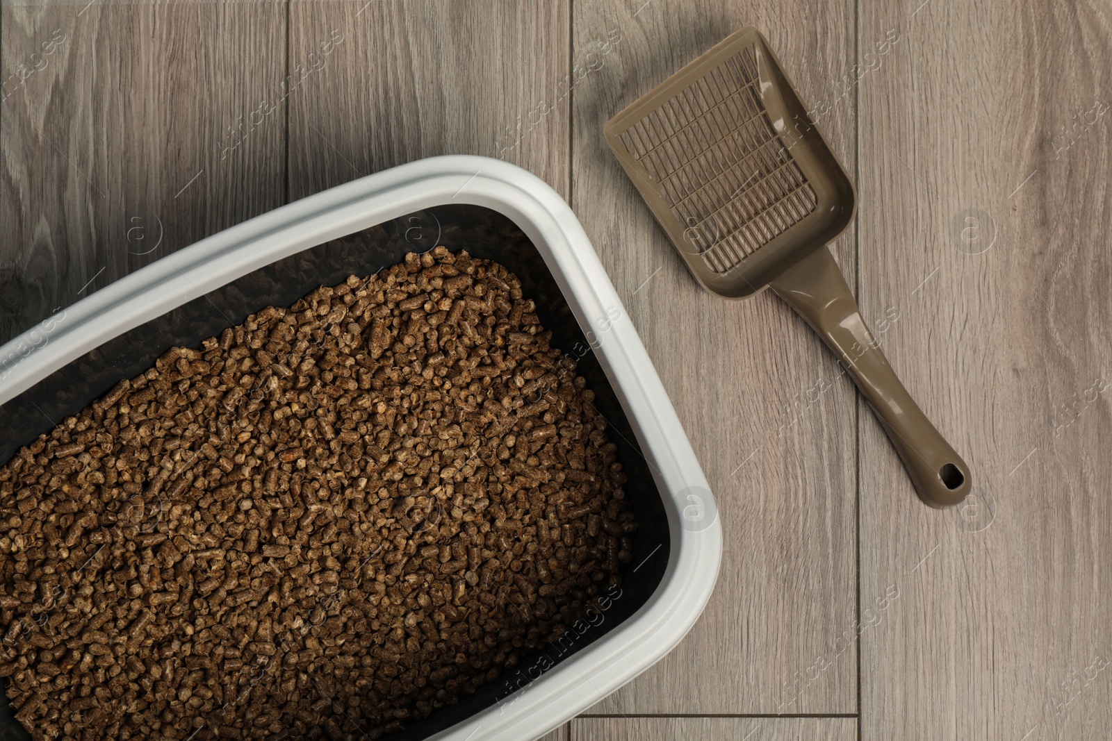 Photo of Cat tray with biodegradable litter and scoop on wooden floor, top view