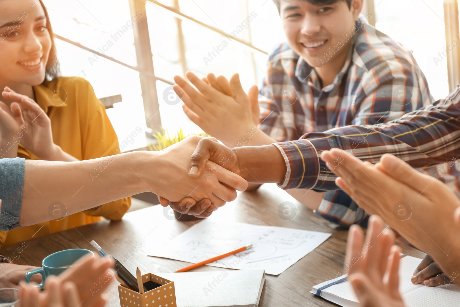 Photo of Young men shaking hands at table. Unity concept