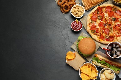 Photo of Pizza, burger and other fast food on black table, flat lay with space for text