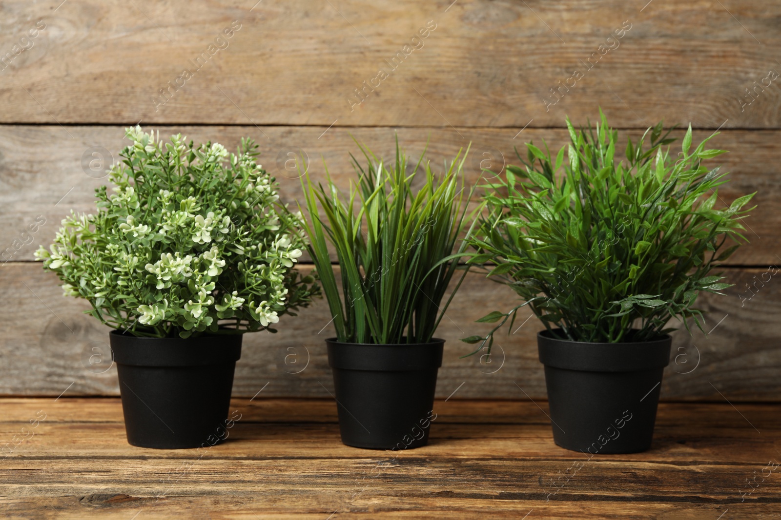 Photo of Artificial plants in black flower pots on wooden table