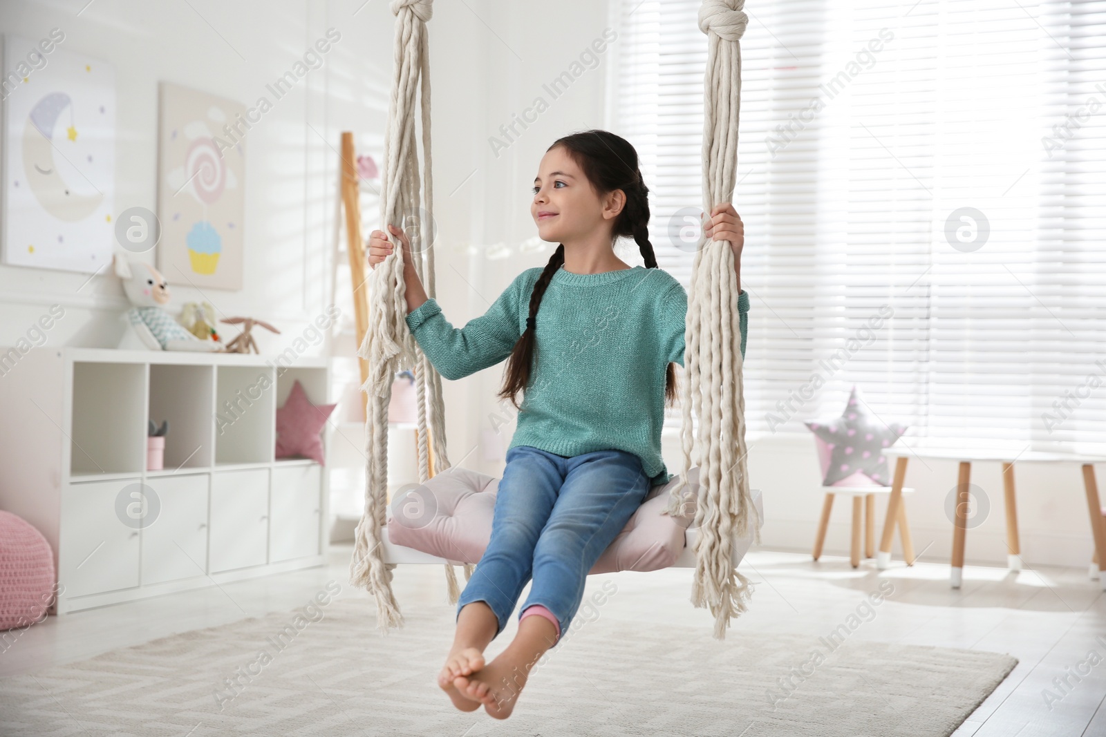 Photo of Cute little girl playing on swing at home