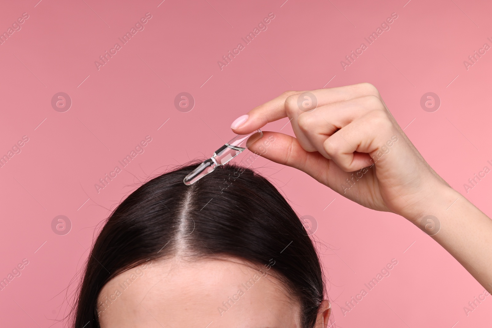 Photo of Beautiful young woman using ampoule for hair treatment on pink background, closeup