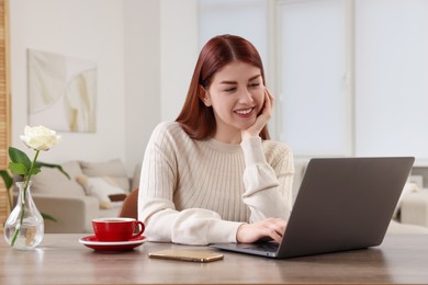 Photo of Happy woman using laptop at wooden table