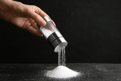 Woman pouring salt from shaker onto black table, closeup