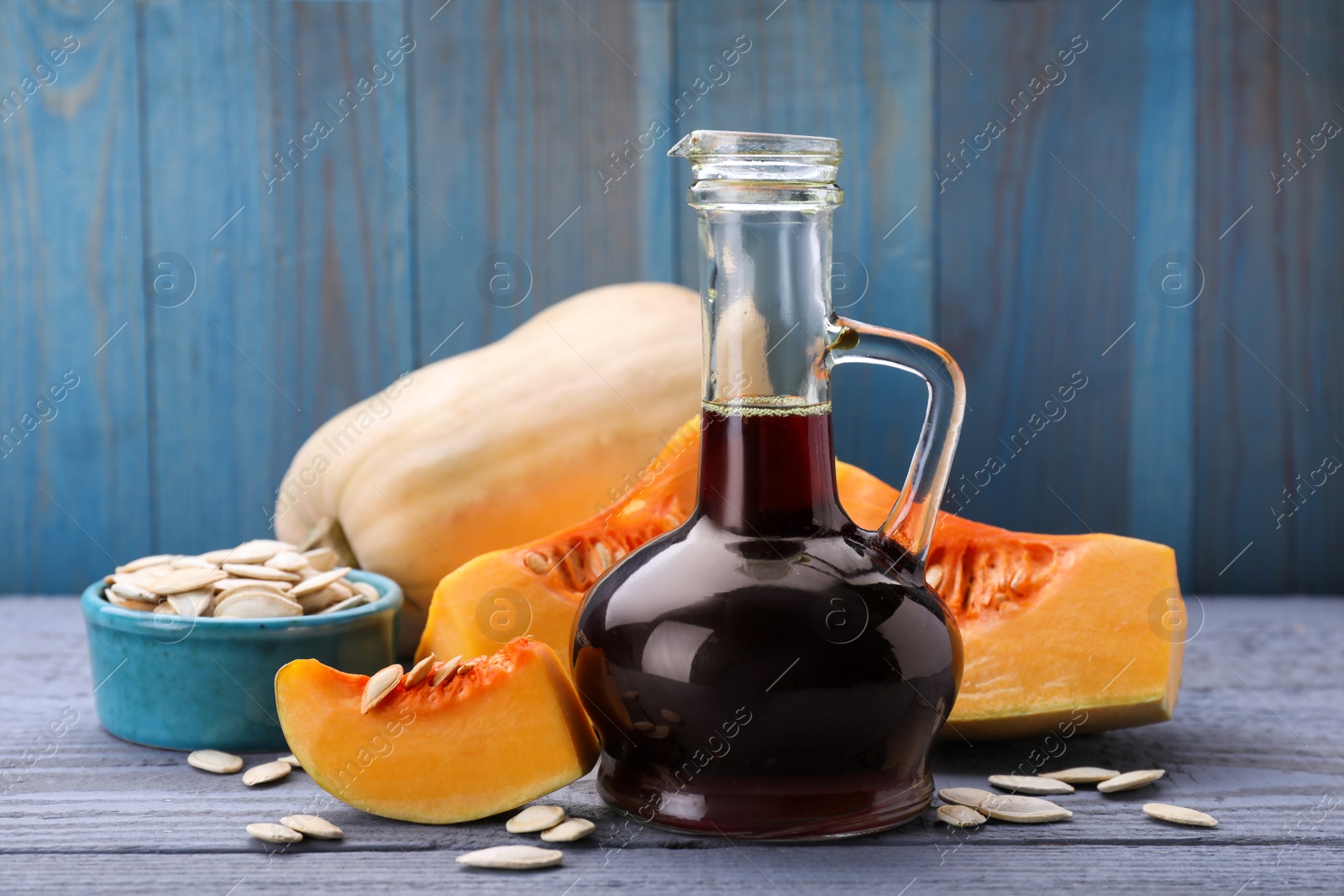 Photo of Fresh pumpkin seed oil in glass jug on grey wooden table