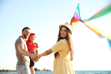 Photo of Happy parents and their child playing with kite near sea. Spending time in nature