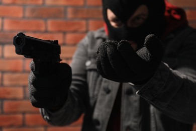 Dangerous criminal with gun near brick wall, selective focus. Armed robbery